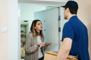 young-displeased-woman-standing-doorway-talking-delivery-man-while-receiving-package