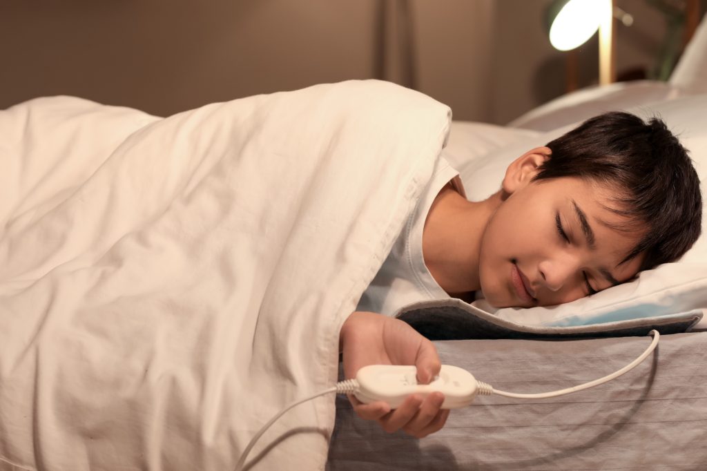 Little boy sleeping on electric heating pad in bedroom at night