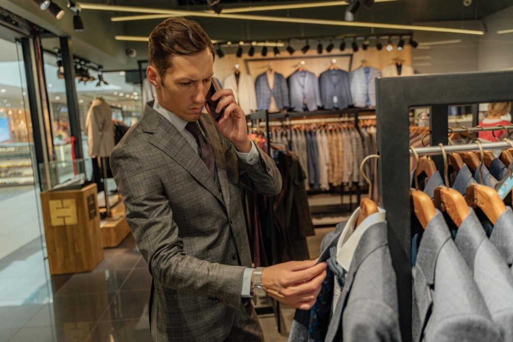 Stylish man browsing suits in a modern clothing store, talking on phone.