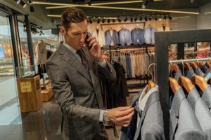 Stylish man browsing suits in a modern clothing store, talking on phone.