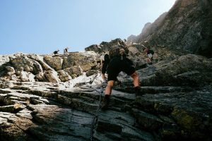 Adventurers climbing a steep, rocky path in the Tatra Mountains under a clear blue sky.