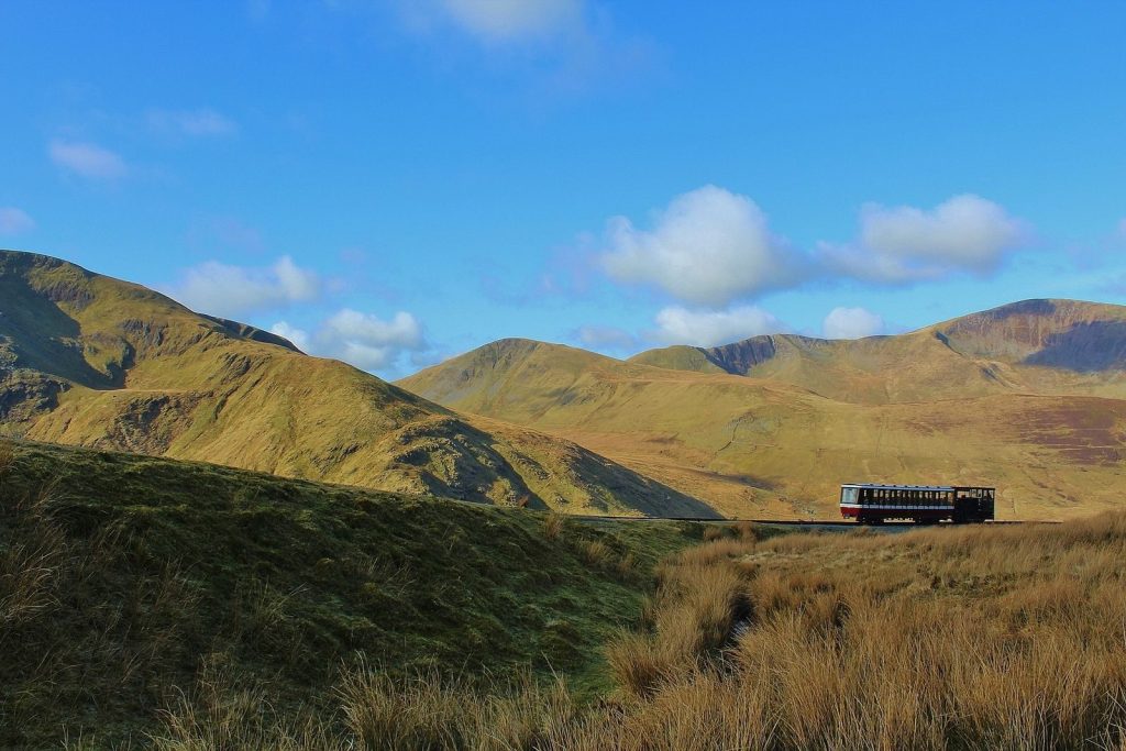 A picturesque train traverses the scenic Snowdonia mountains under a clear blue sky in Gwynedd, Wales.