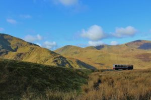 A picturesque train traverses the scenic Snowdonia mountains under a clear blue sky in Gwynedd, Wales.